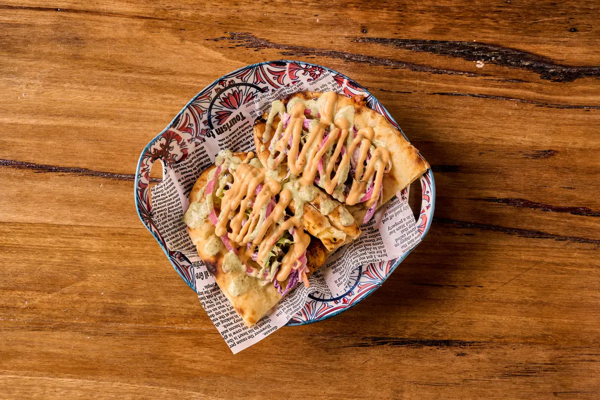 Folded naan with shredded vegetables, pink onions and sauces on a patterned plate.